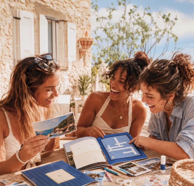 Trois femmes sourient autour d'une table avec des souvenirs de vacances.